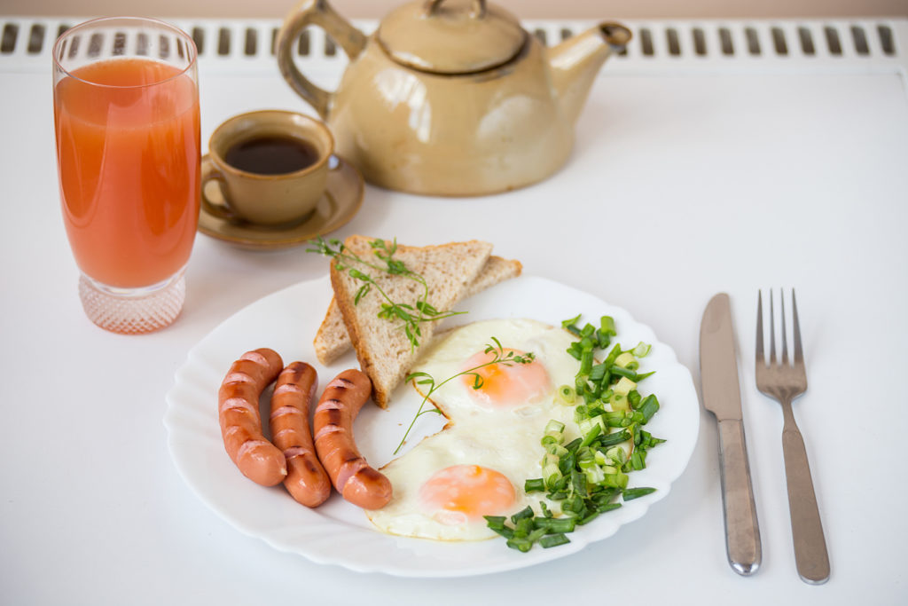 Fried eggs with sausages and bread on the white plate with glass of juice and a cup of coffee