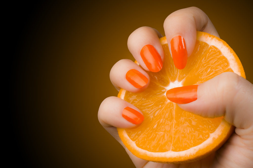 Female hand with orange nails holds an orange fruit.
