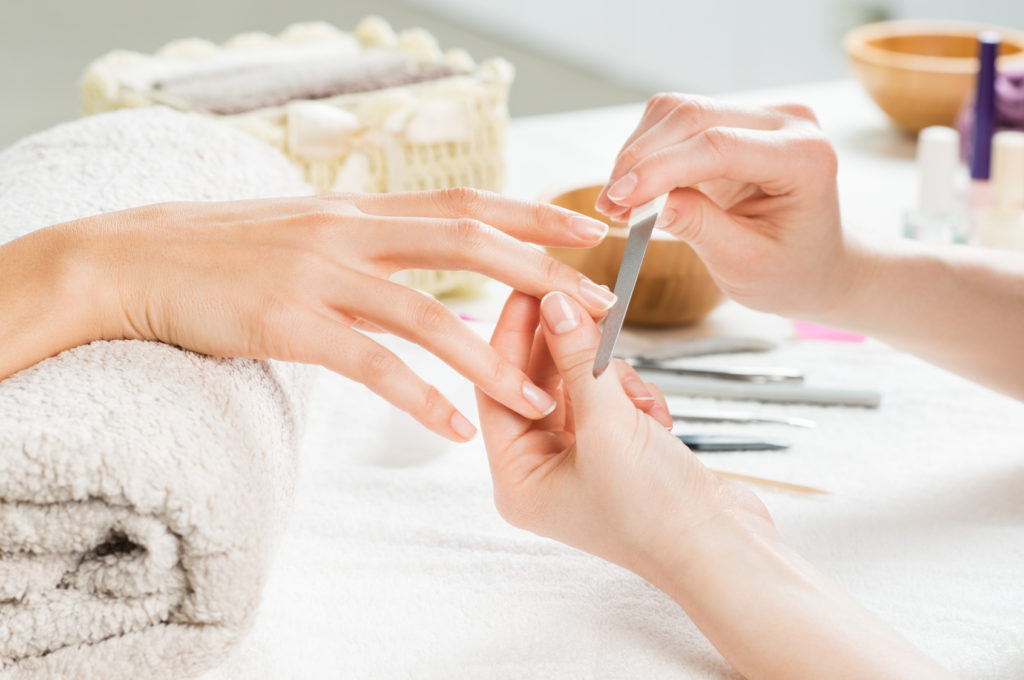 Closeup shot of a woman in a nail salon receiving a manicure by a beautician with nail file. Woman getting nail manicure. Beautician file nails to a customer. Shallow depth of field with focus on nailfile.